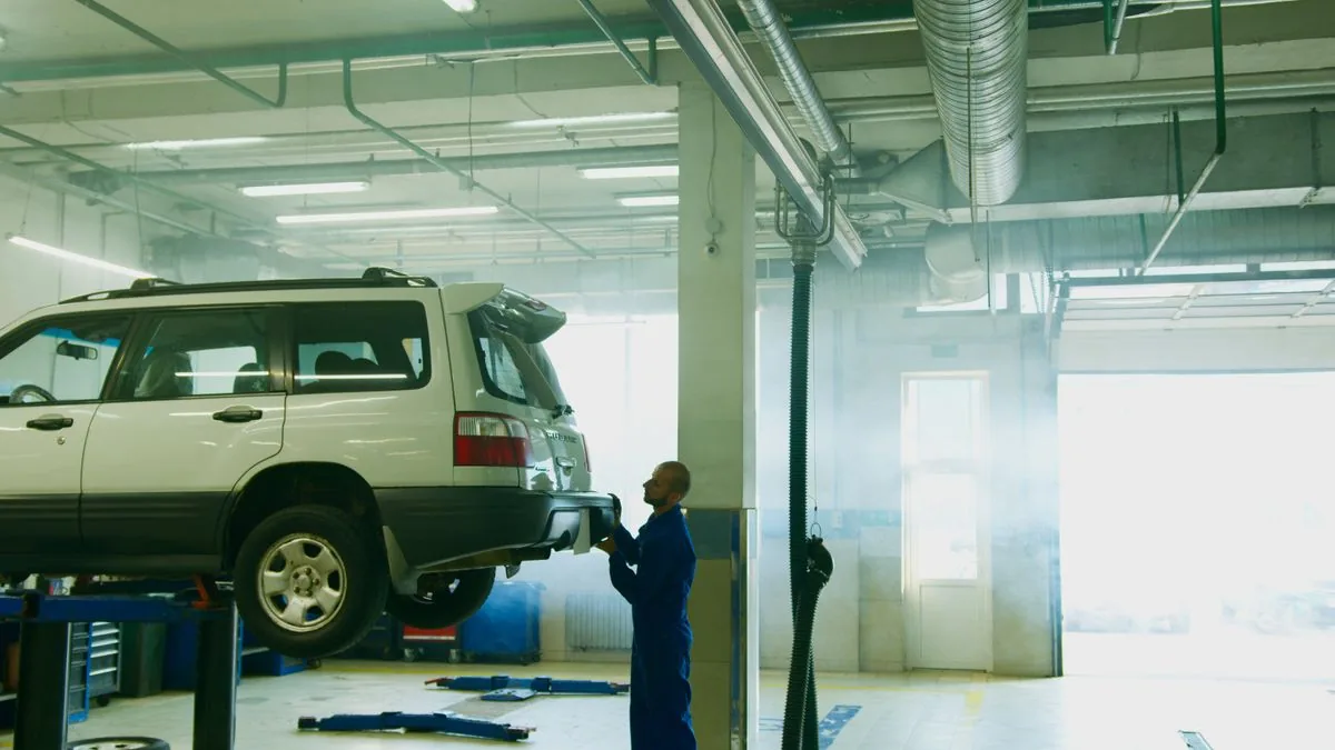 A car up on the lift in a bright vehicle workshop, a technician working underneath
